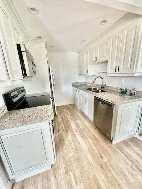 kitchen with sink, white cabinetry, appliances with stainless steel finishes, light stone countertops, and light hardwood / wood-style floors