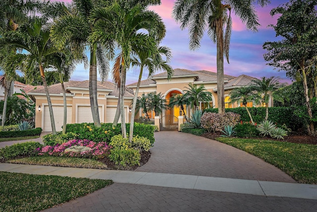 mediterranean / spanish-style house featuring an attached garage, a tile roof, decorative driveway, a gate, and stucco siding