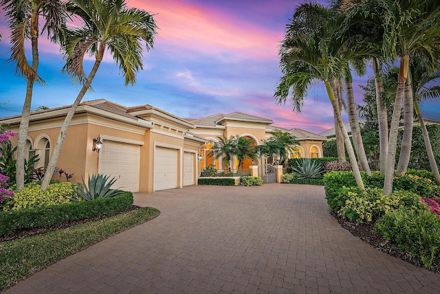 mediterranean / spanish-style house featuring a garage, decorative driveway, a tile roof, and stucco siding