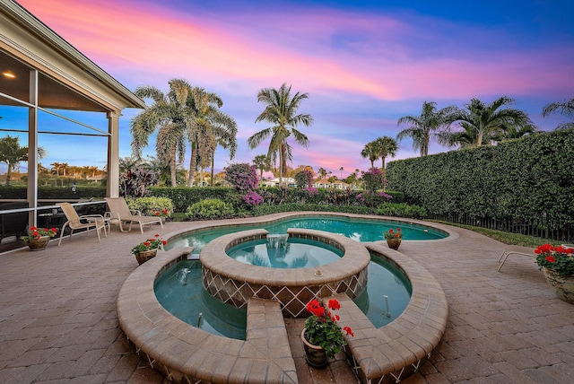 pool at dusk with an in ground hot tub and a patio area