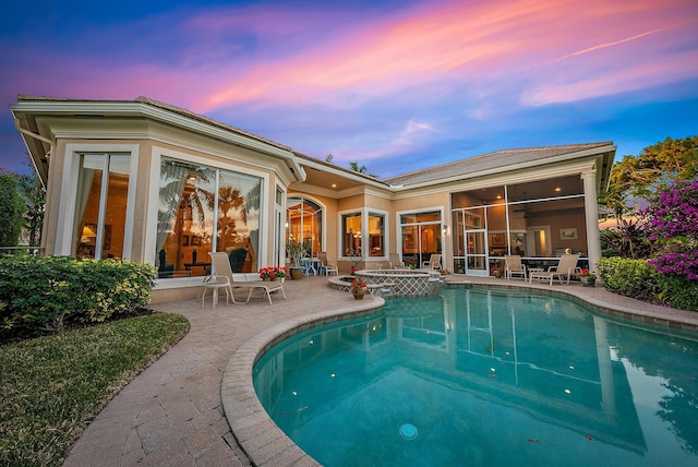 pool at dusk featuring an in ground hot tub and a patio