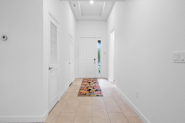 hallway featuring a tray ceiling, light tile patterned floors, and a towering ceiling