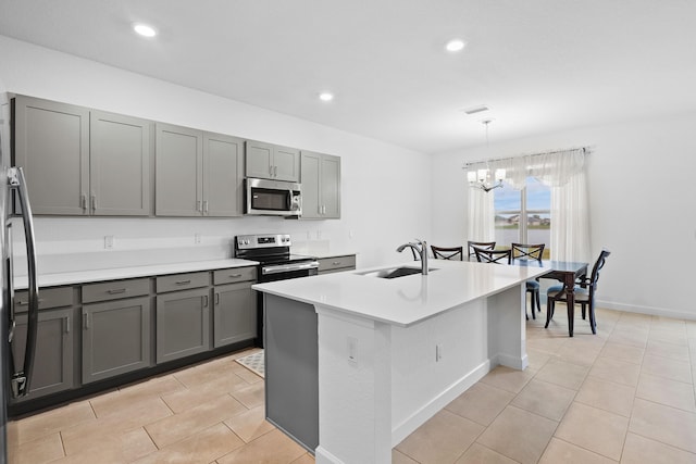 kitchen with sink, gray cabinetry, stainless steel appliances, a center island with sink, and decorative light fixtures