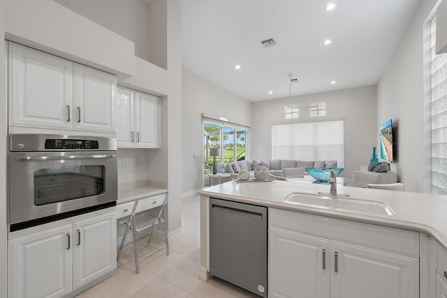 kitchen featuring sink, light tile patterned floors, appliances with stainless steel finishes, white cabinetry, and decorative light fixtures