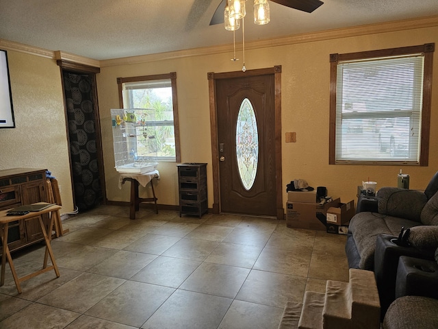 tiled entrance foyer featuring a textured ceiling, a ceiling fan, and crown molding