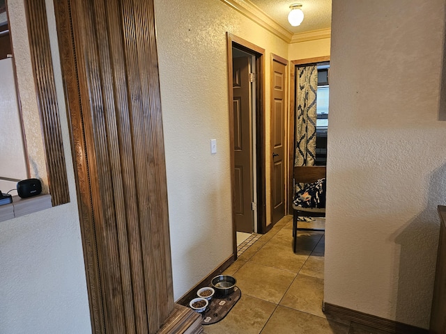 hallway featuring light tile patterned floors, baseboards, crown molding, and a textured wall