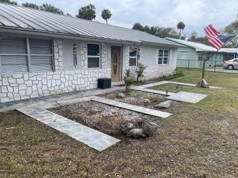 single story home with stone siding, metal roof, a standing seam roof, fence, and a front lawn