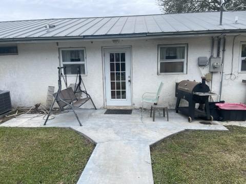 entrance to property with metal roof, a lawn, stucco siding, a standing seam roof, and a patio area