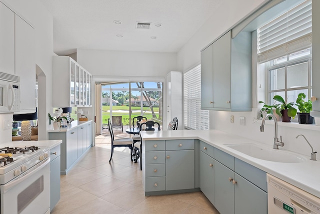 kitchen with light tile patterned flooring, sink, gray cabinetry, kitchen peninsula, and white appliances