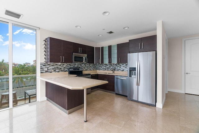 kitchen featuring appliances with stainless steel finishes, a breakfast bar, expansive windows, kitchen peninsula, and dark brown cabinets