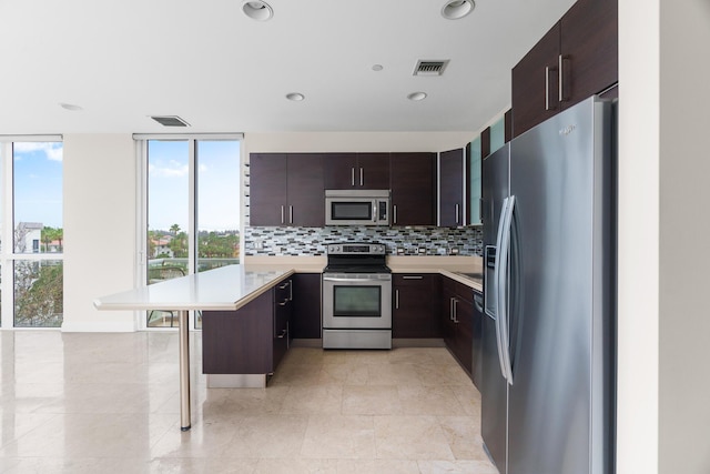 kitchen with dark brown cabinetry, a kitchen bar, decorative backsplash, and appliances with stainless steel finishes