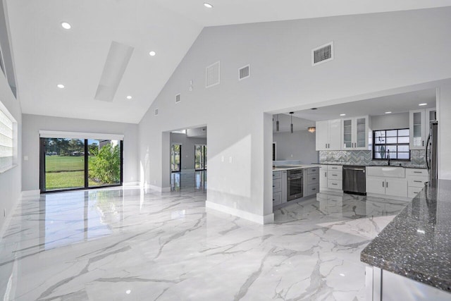 kitchen with sink, white cabinetry, stainless steel appliances, decorative backsplash, and dark stone counters