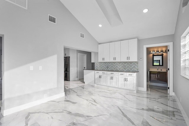 kitchen featuring backsplash, black refrigerator, high vaulted ceiling, and white cabinets