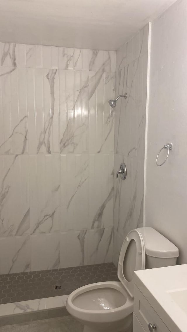 bathroom featuring a tile shower, vanity, and toilet