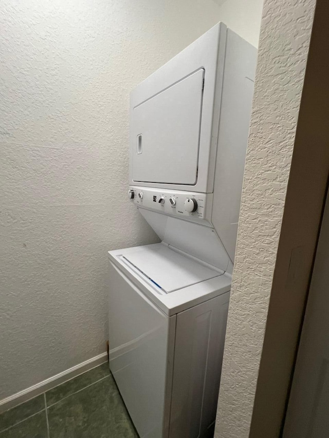 washroom with dark tile patterned flooring and stacked washer / drying machine