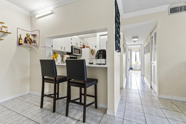 kitchen featuring kitchen peninsula, a kitchen breakfast bar, white refrigerator, white cabinets, and light tile patterned floors