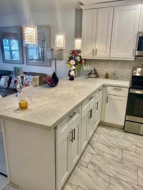 kitchen with tasteful backsplash, white cabinets, hanging light fixtures, kitchen peninsula, and stainless steel appliances