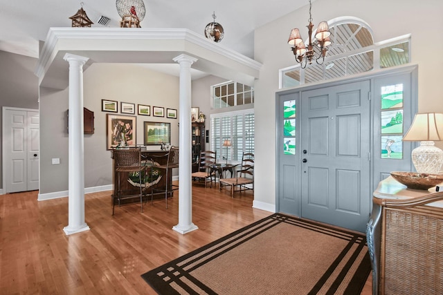 foyer featuring wood finished floors, a towering ceiling, baseboards, decorative columns, and an inviting chandelier