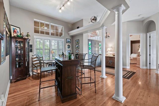 dining space with a towering ceiling, baseboards, light wood-style flooring, and ornate columns