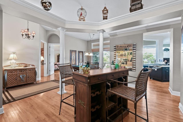 interior space with baseboards, light wood-type flooring, ornate columns, an inviting chandelier, and crown molding