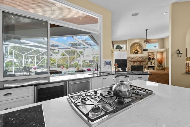 kitchen with wine cooler, a fireplace, a sink, appliances with stainless steel finishes, and dark stone countertops