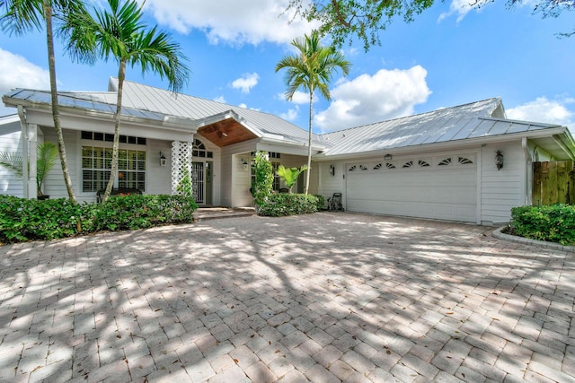 ranch-style house with an attached garage, a standing seam roof, metal roof, and decorative driveway