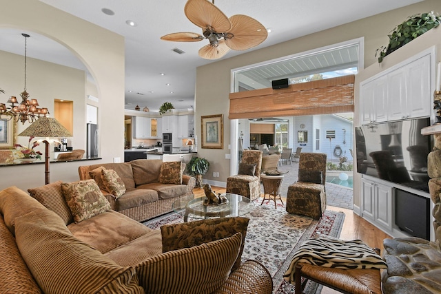 living area featuring light wood-style flooring, recessed lighting, ceiling fan with notable chandelier, visible vents, and a towering ceiling