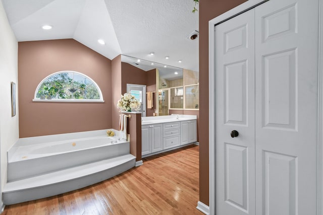 full bathroom with a closet, a stall shower, vaulted ceiling, vanity, and a bath