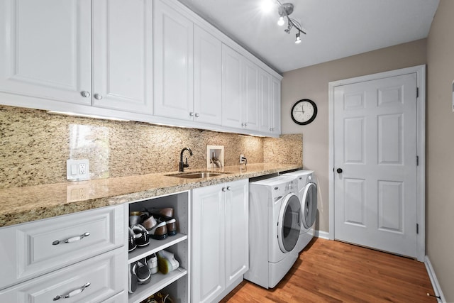 washroom with light wood-style flooring, separate washer and dryer, a sink, baseboards, and cabinet space