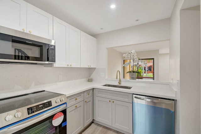 kitchen with sink, backsplash, stainless steel appliances, white cabinets, and light wood-type flooring