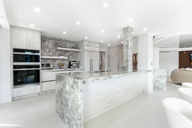 kitchen with sink, light tile patterned floors, paneled built in refrigerator, black double oven, and light stone countertops