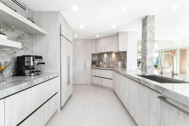 kitchen with sink, paneled built in refrigerator, backsplash, light stone counters, and light brown cabinets