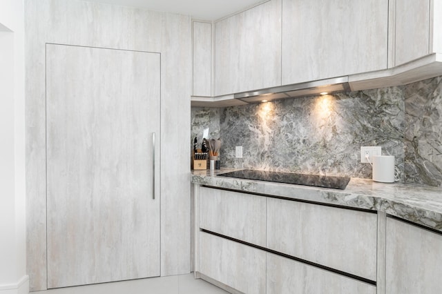 kitchen featuring light stone countertops, black electric stovetop, wall chimney exhaust hood, and decorative backsplash