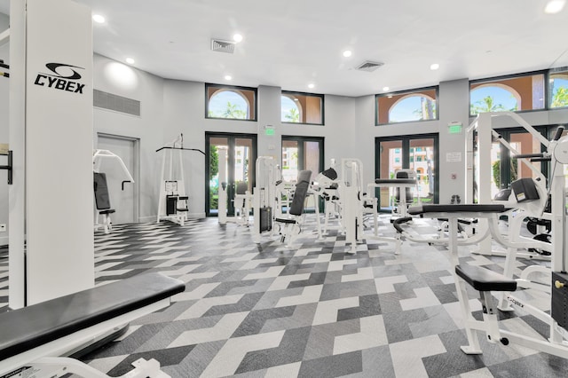 gym featuring a towering ceiling, french doors, and carpet flooring