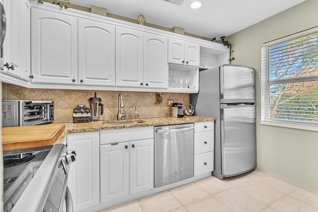 kitchen with light tile patterned floors, tasteful backsplash, appliances with stainless steel finishes, white cabinetry, and a sink