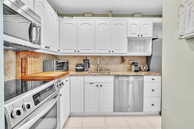 kitchen featuring light tile patterned flooring, a sink, white cabinetry, appliances with stainless steel finishes, and decorative backsplash