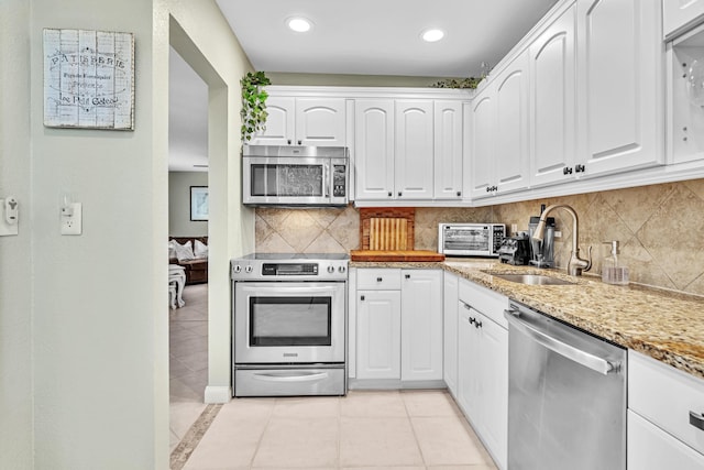 kitchen featuring light tile patterned flooring, stainless steel appliances, a sink, white cabinets, and light stone countertops