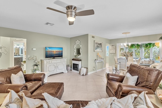 living area with light tile patterned flooring, ceiling fan with notable chandelier, a fireplace, visible vents, and baseboards