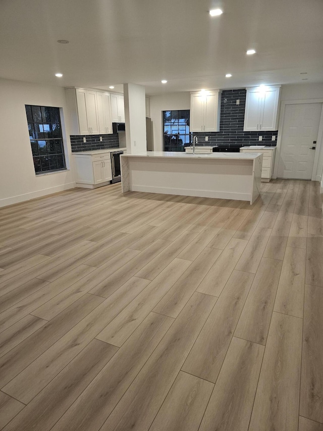 kitchen with sink, light hardwood / wood-style flooring, white cabinetry, backsplash, and a kitchen island