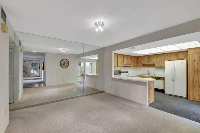 kitchen featuring sink, white appliances, a textured ceiling, light colored carpet, and kitchen peninsula