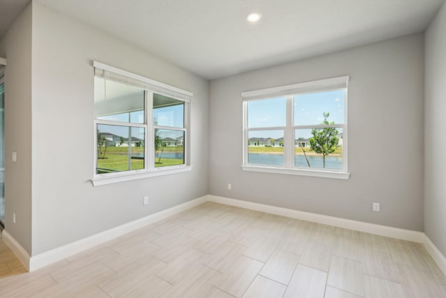 empty room featuring recessed lighting, a water view, and baseboards