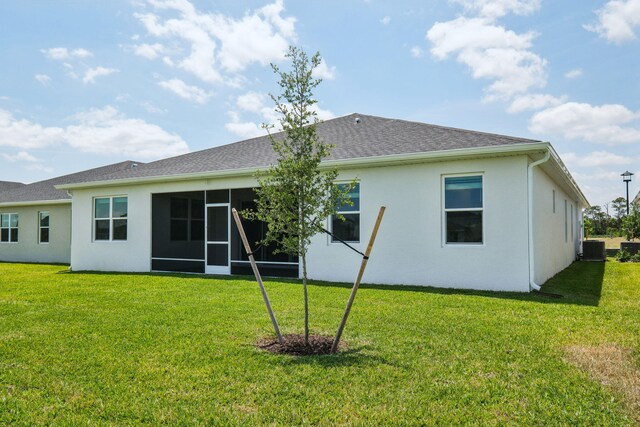 rear view of property with a sunroom, cooling unit, a lawn, roof with shingles, and stucco siding