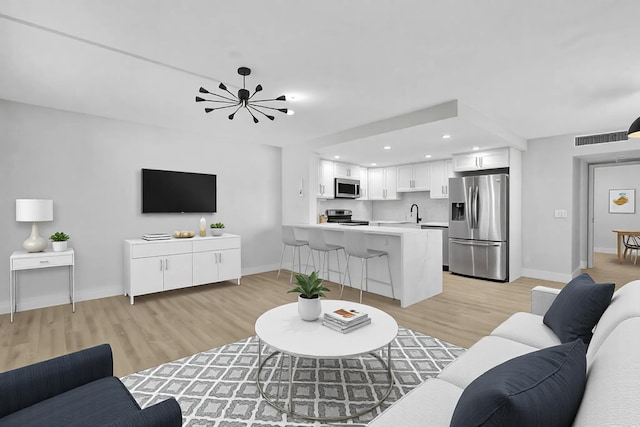 living room with a chandelier, light wood finished floors, visible vents, and baseboards