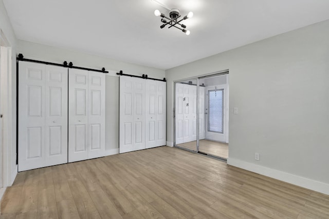 unfurnished bedroom featuring light wood-type flooring, a barn door, baseboards, and two closets