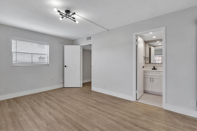 unfurnished bedroom featuring sink, ensuite bath, and light hardwood / wood-style flooring