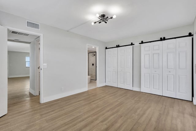 unfurnished bedroom featuring light wood-type flooring, a barn door, visible vents, and multiple closets