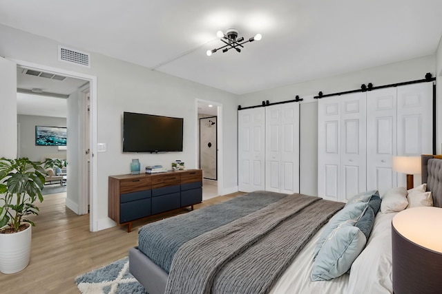 bedroom with a barn door, visible vents, light wood-style flooring, and two closets