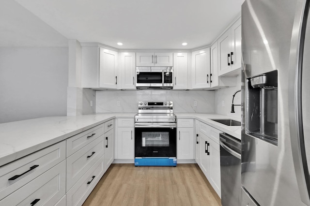 kitchen featuring stainless steel appliances, white cabinetry, sink, and light stone counters