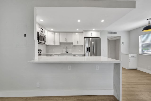 kitchen featuring stainless steel appliances, a peninsula, a sink, visible vents, and light wood-type flooring