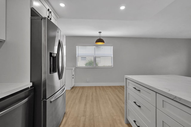 kitchen featuring light stone counters, appliances with stainless steel finishes, hanging light fixtures, and light hardwood / wood-style flooring